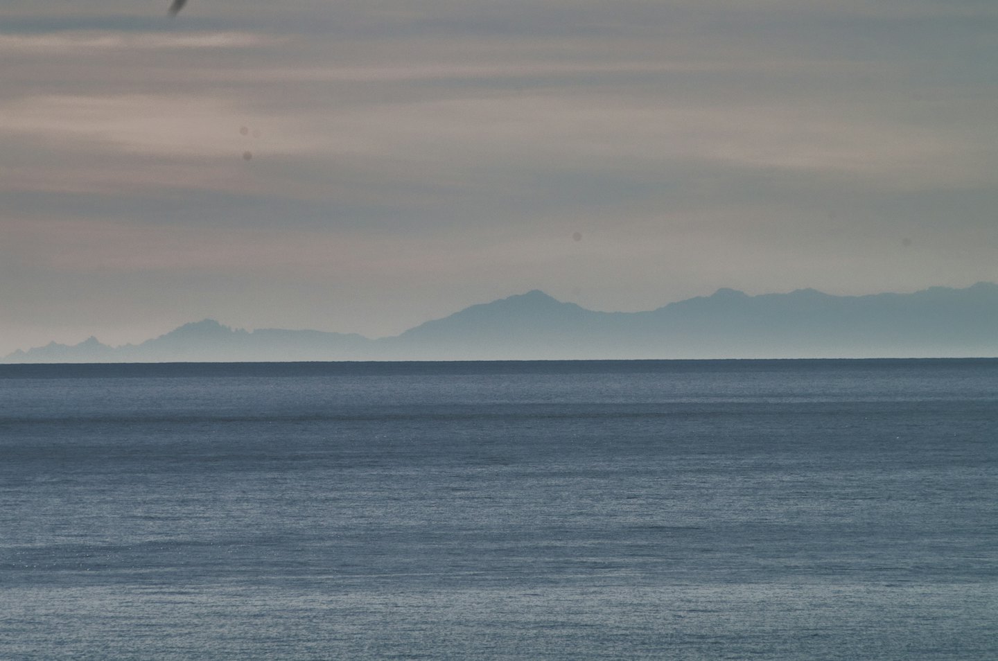 Montagne lontane si ergono sopra un calmo oceano blu scuro.