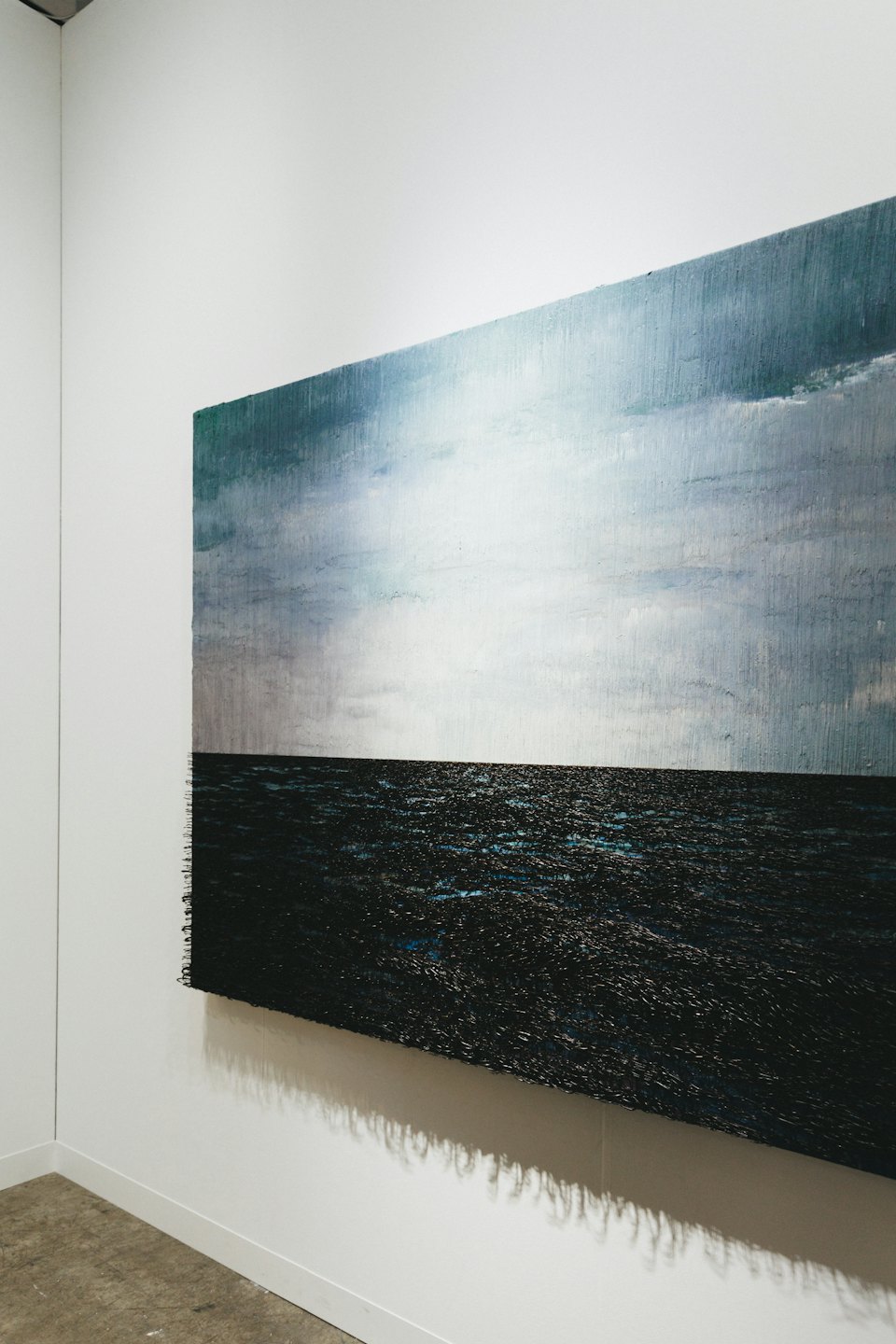 Dipinto astratto materico dell'oceano appeso a una parete bianca da galleria.